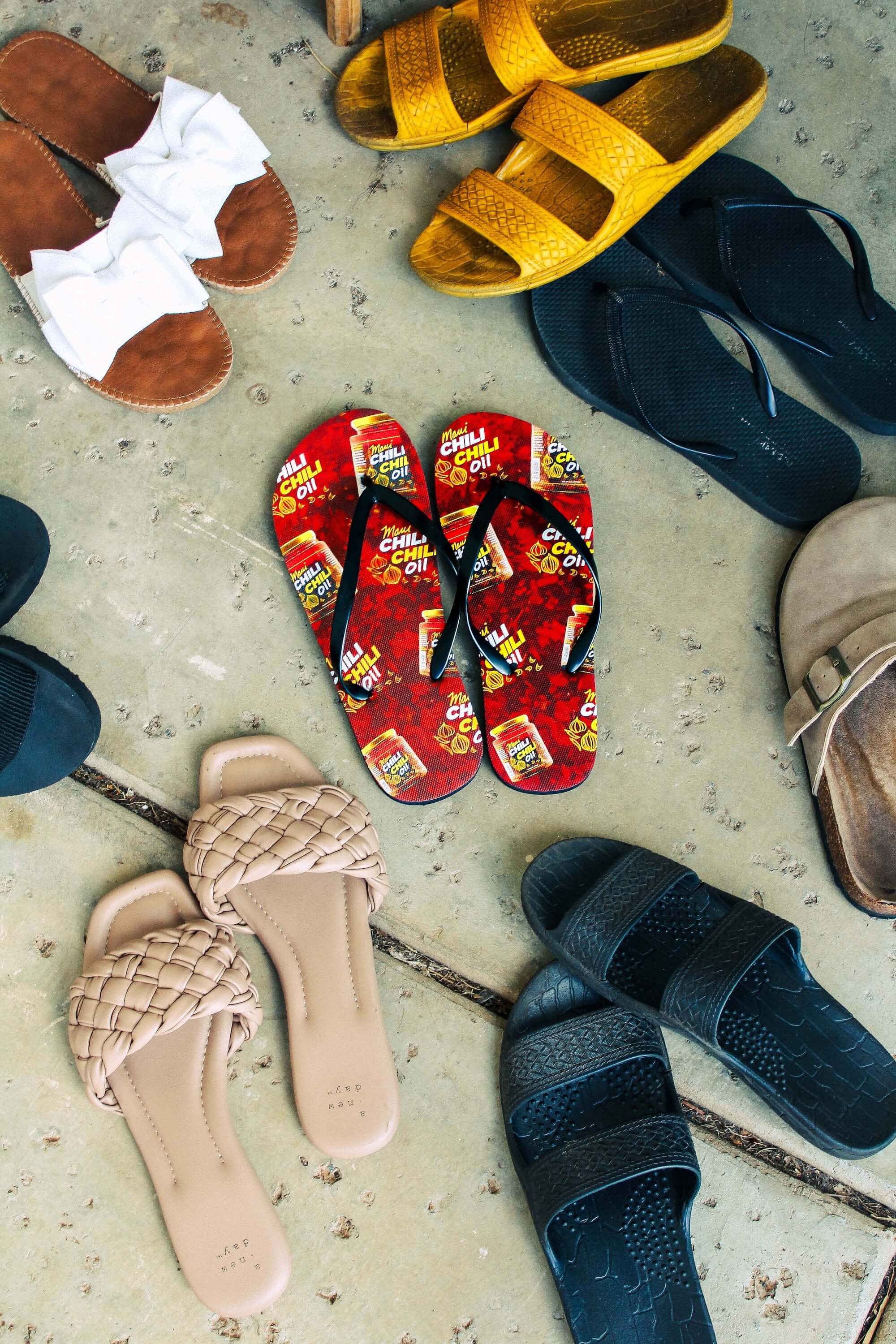Various pairs of sandals including red flip-flops on a concrete floor.