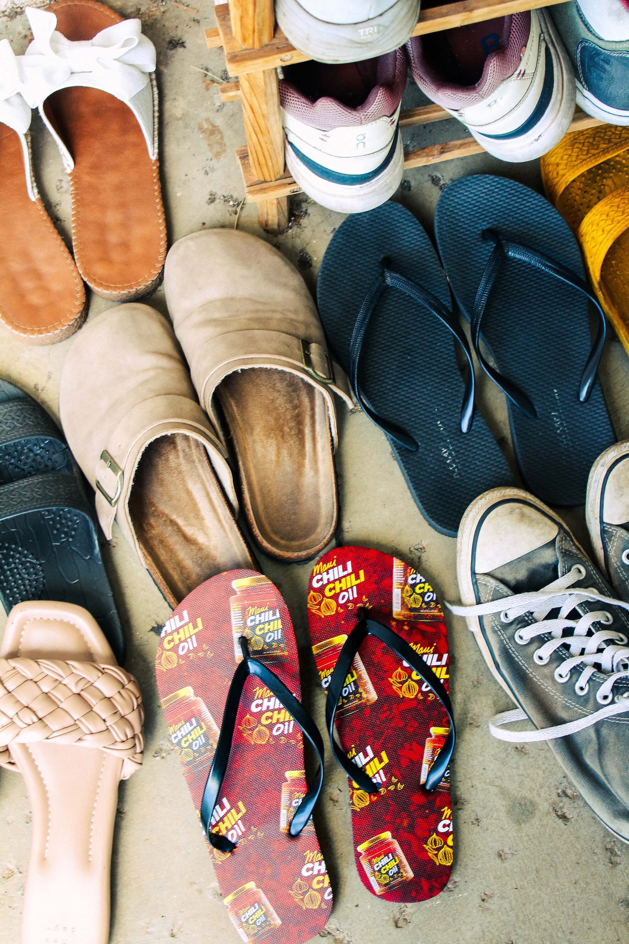 Collection of various shoes including sandals, slippers, and sneakers on a concrete surface.