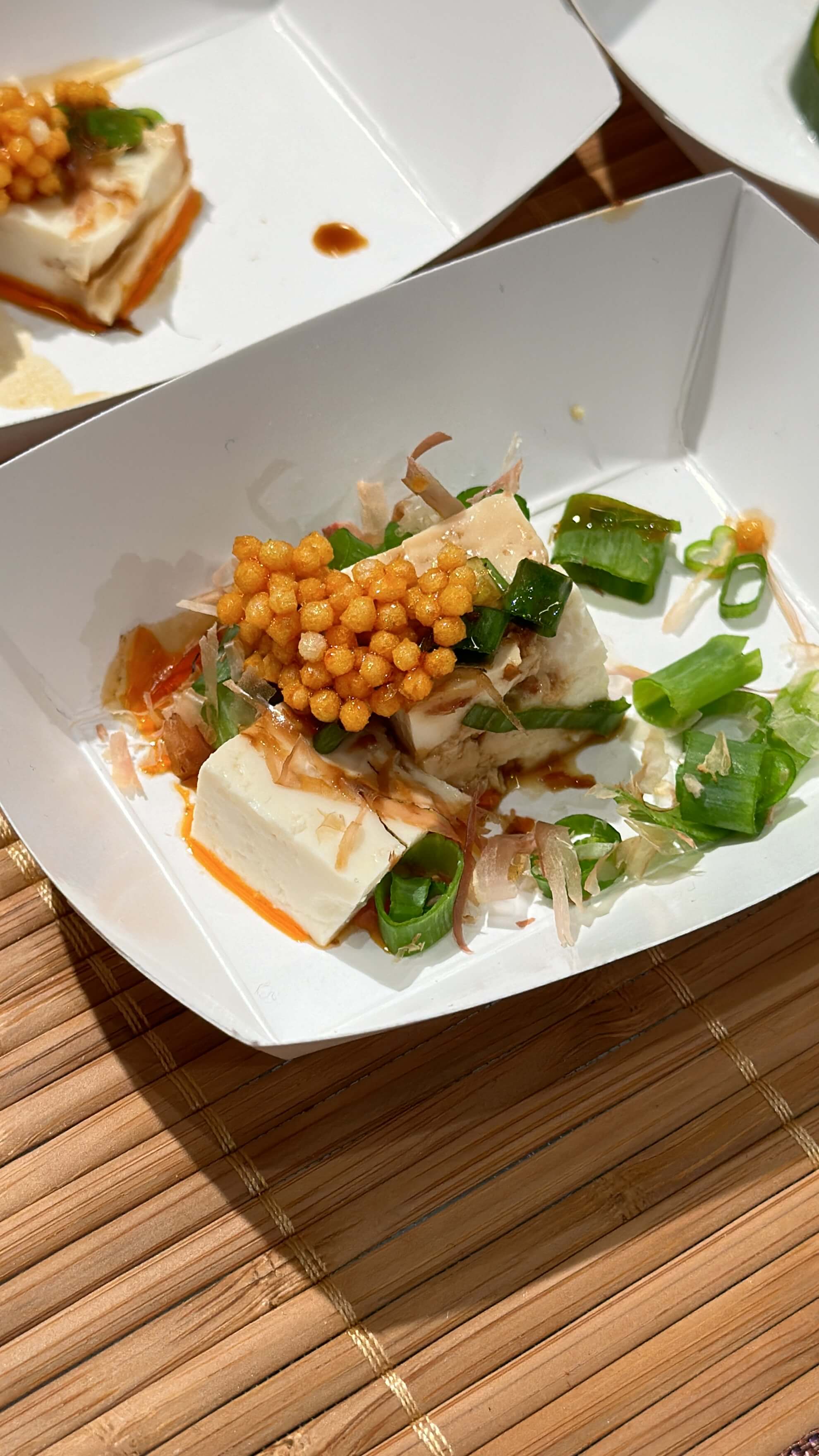Plated dish with tofu and vegetables and bubu arare drizzled on top on a wooden surface