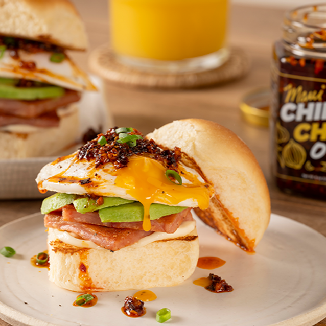 Delicious breakfast slider with egg, ham, and cheese on a bun, served with a glass of orange juice and Maui Chili Oil.