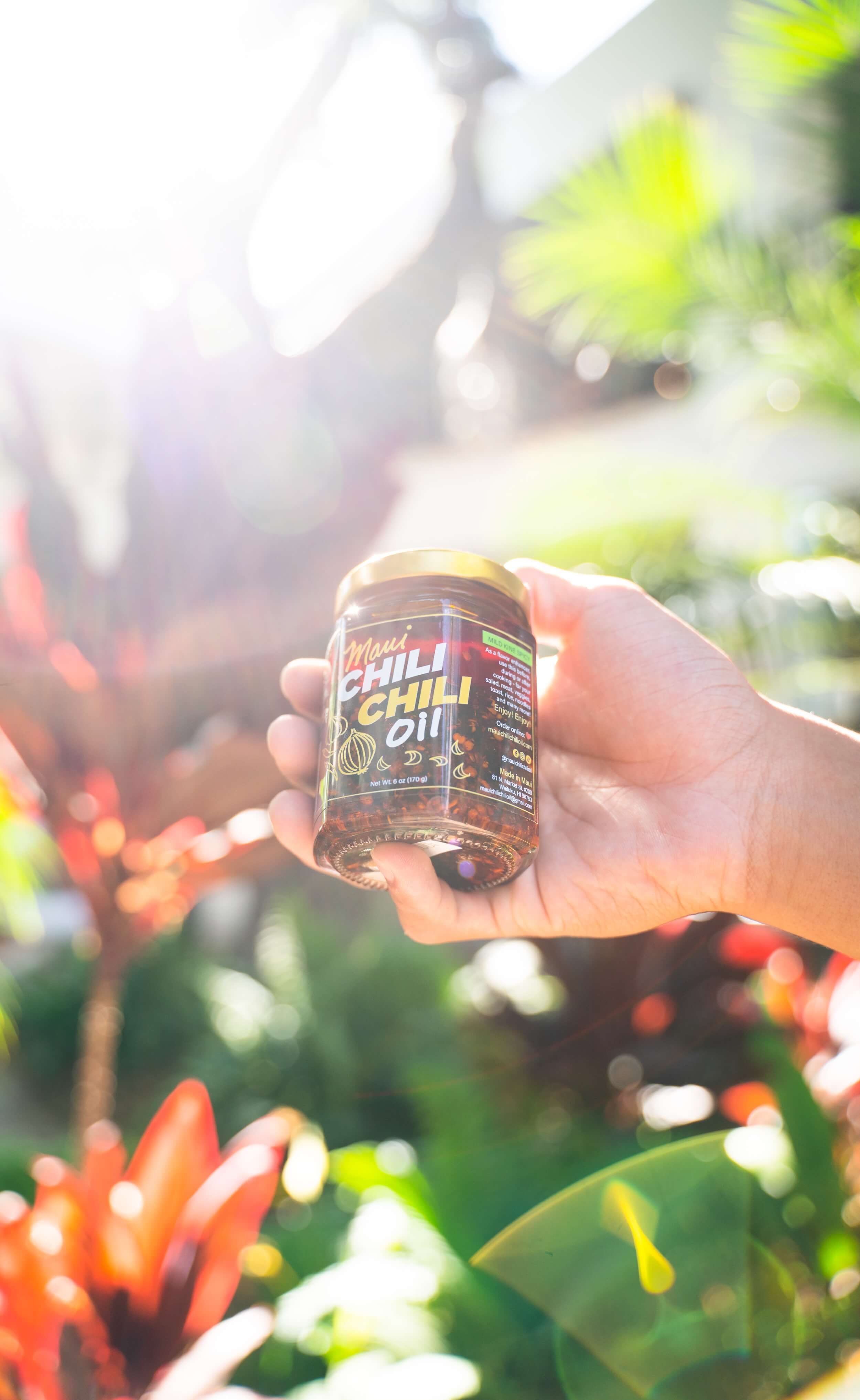 Hand holding a bottle of chili oil with a blurred natural background