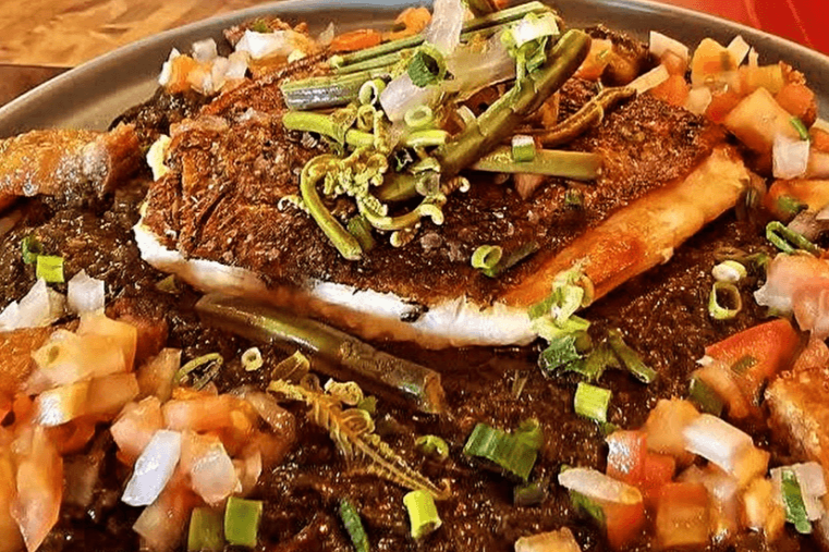 Plated dish of grilled fish with garnishes on a wooden table