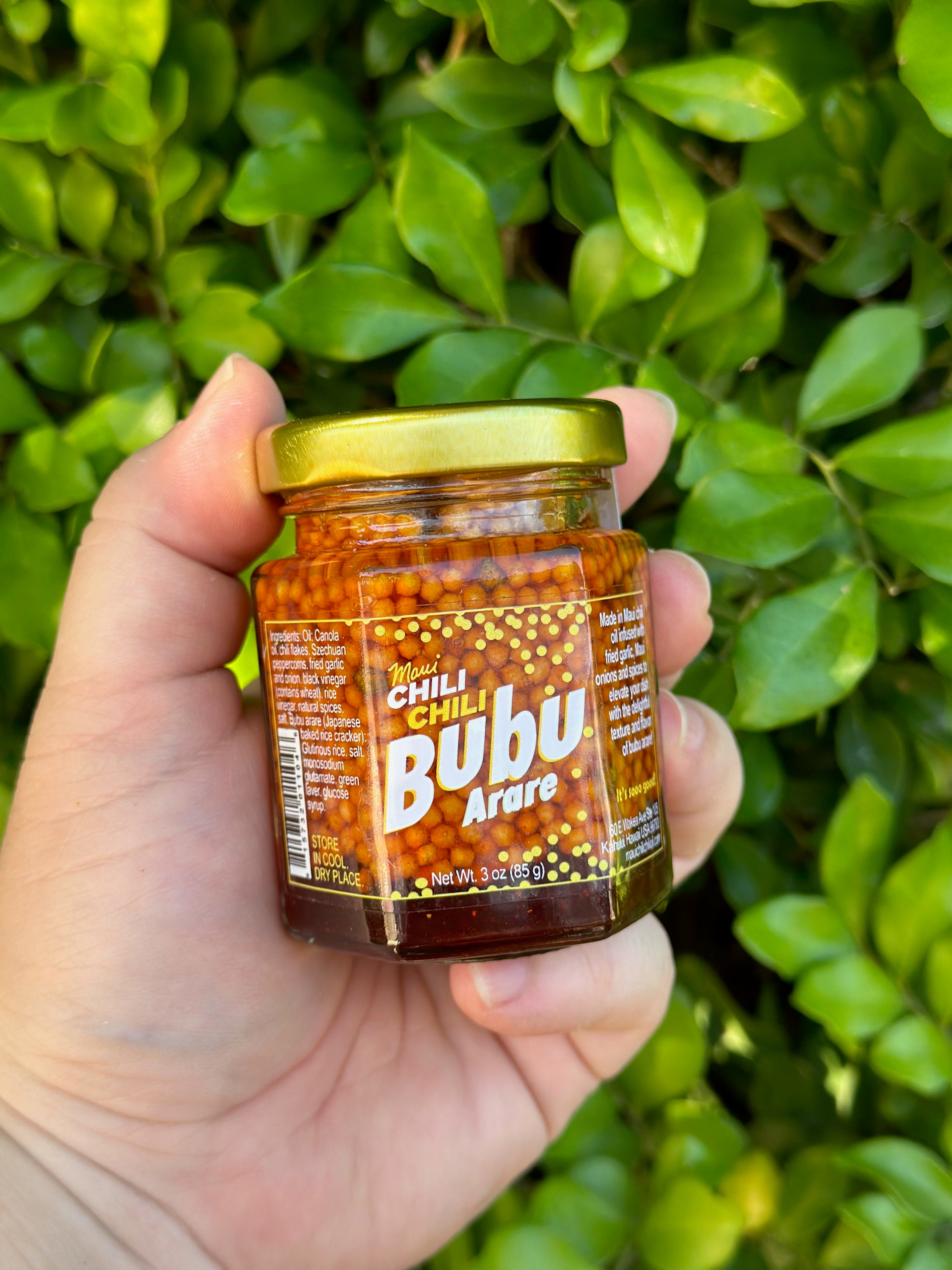 hand holding jar of bubu arare in front of green leafy backdrop