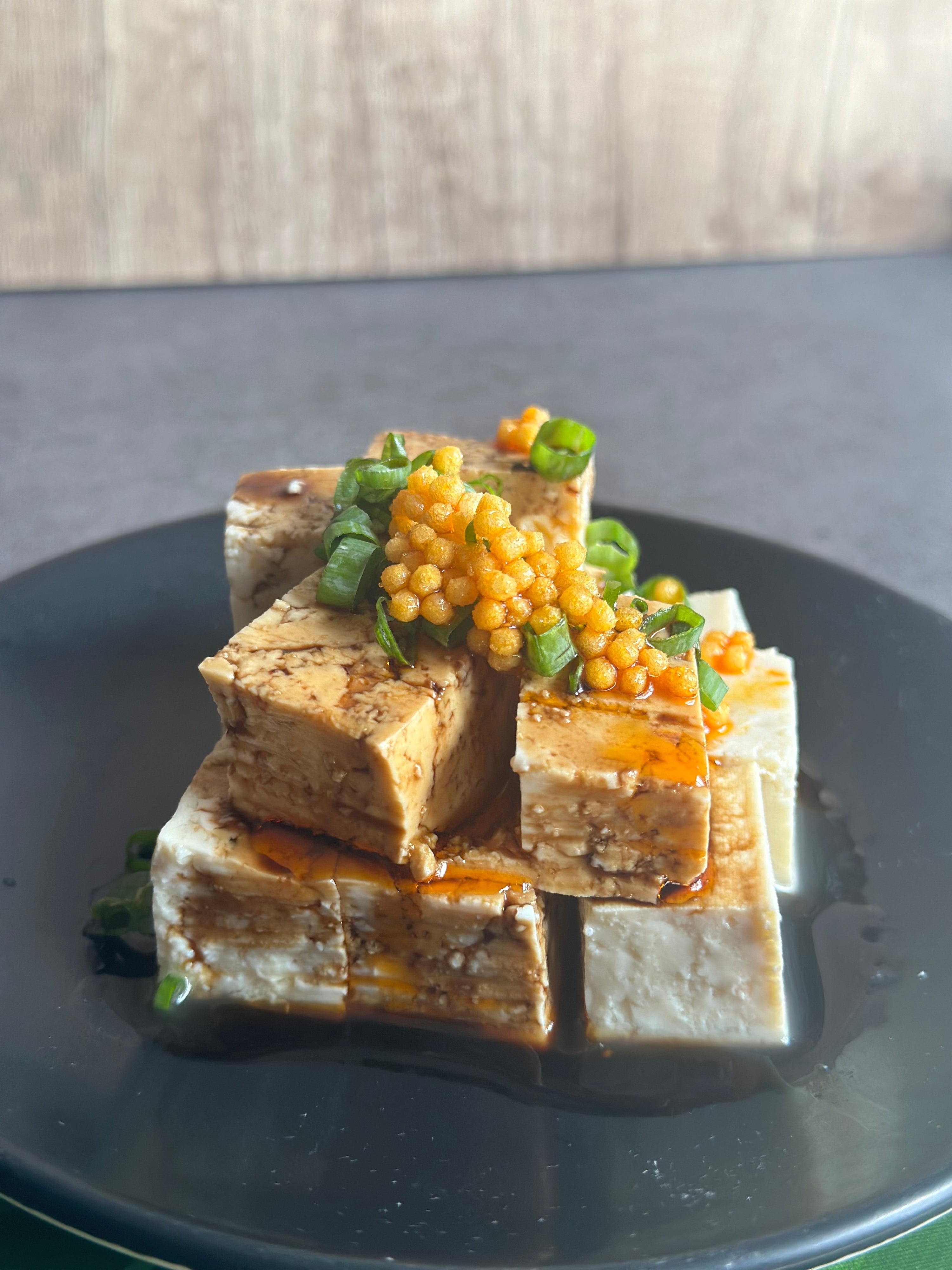 tofu dish with green onions and bubu arare on top on a black plate