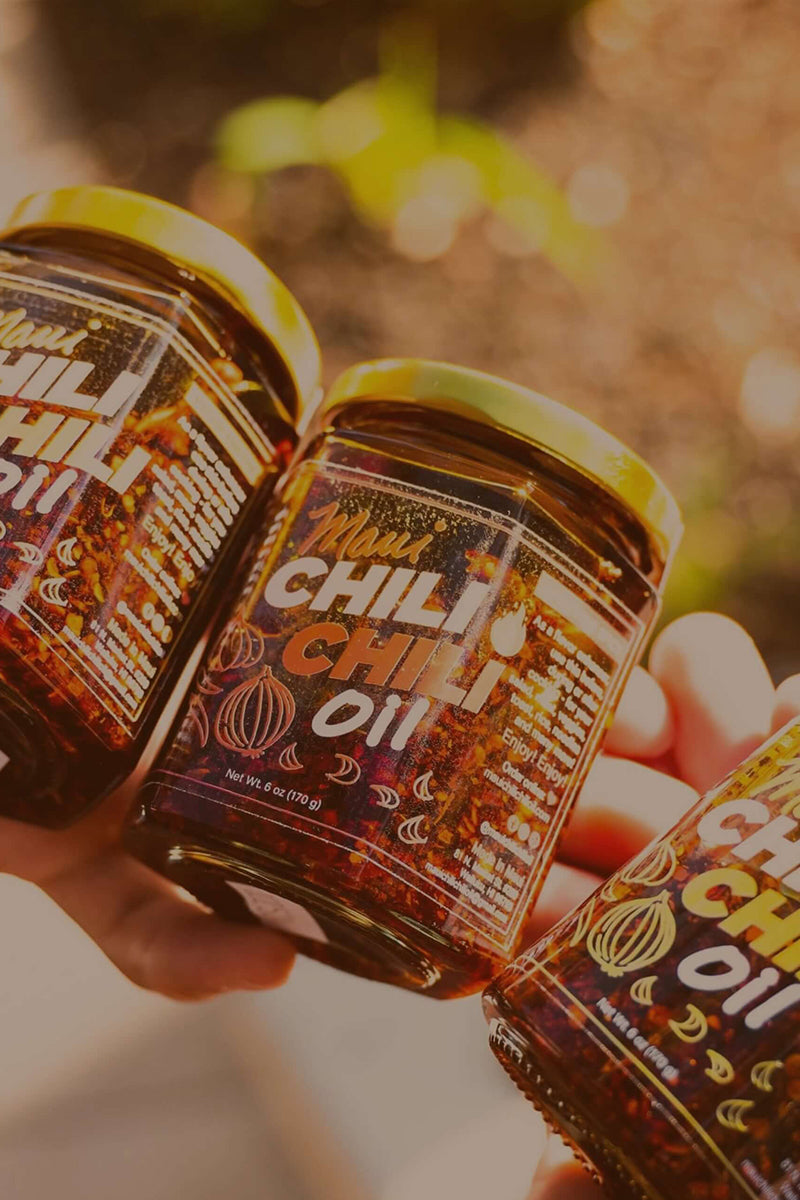 Three bottles of chili oil held by a person with a blurred natural background