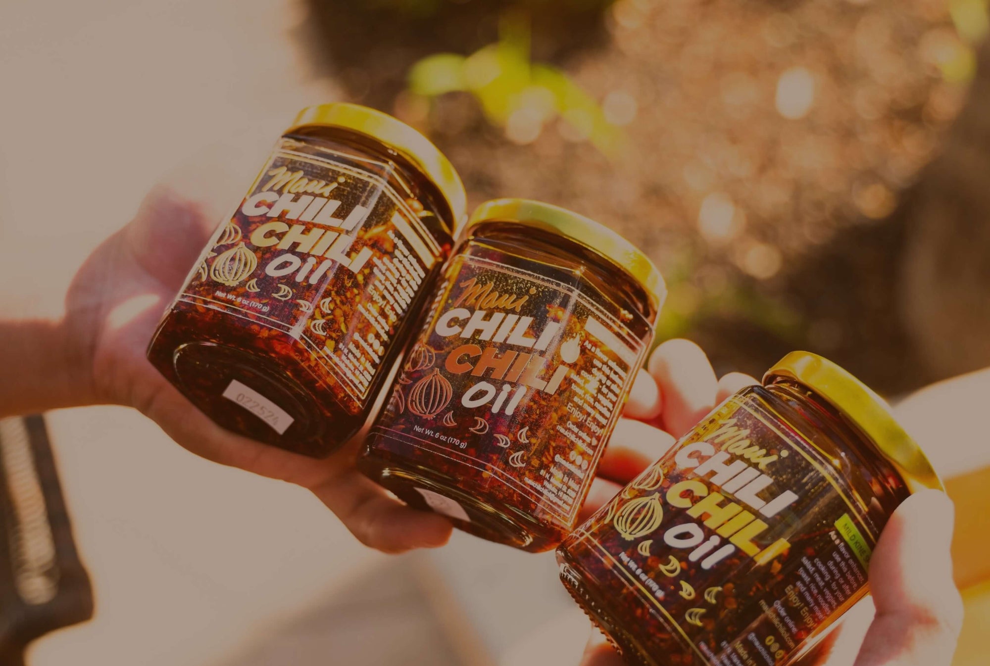 Three jars of chili oil being held together with a blurred natural background
